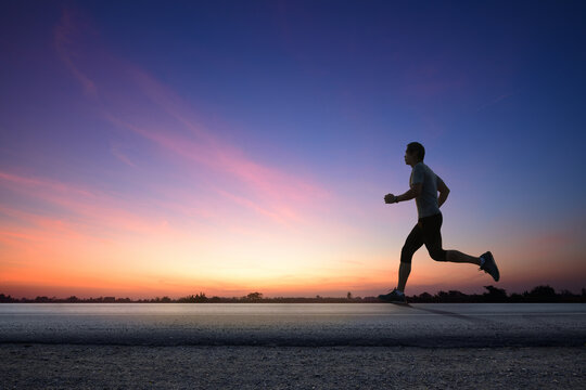 Silhouette view of a man jogging on road with dawn sky background.