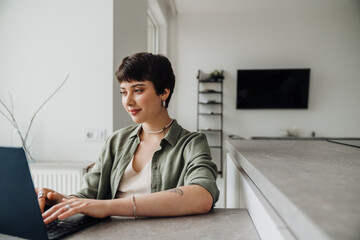 Smiling woman working on laptop while sitting at table at home