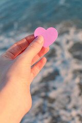 The lilac heart in the hand of the girl against the background of waves and sea foam