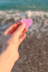 The lilac heart in the hand of the girl against the background of waves and sea foam