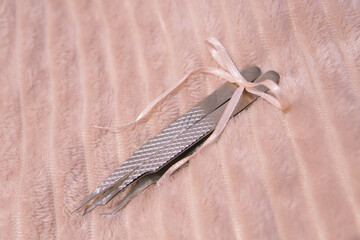Close up of flat and curved metal tweezers for eyelash extensions in hand on pink background with bow