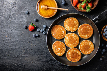 Pancakes in a frying pan with fresh berries and honey. 