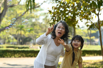 Grandmother and granddaughter having fun blowing soap bubbles into the air in. Family, generation and people concept.