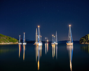 Night view  illuminated white boats located over horizon, colorful lights coming from yachts reflect on the surface of the the Gulf sea. Shot at blue hour in Agios Stefanos Harbour, Corfu , Greece