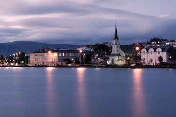 Fototapeta na wymiar An evening long exposure landscape of Reykjavik city centre with Fríkirkjan church over the Tjörnin lake with blurry clouds on the sky and light reflections on the water