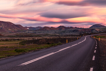 Long exposure Sunset landscape over Iceland red mountains with a clear road on the foreground, blurry orange and purple clouds on the sky
