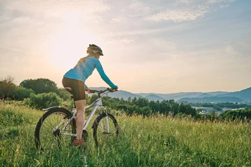 Fotobehang Cyclist Woman riding bike in helmets go in sports outdoors on sunny day a mountain in the forest. Silhouette female at sunset. Fresh air. Health care, authenticity, sense of balance and calmness.  © Andrii IURLOV