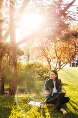 Portrait of attractive cheerful focused businesswoman with wireless headphones working online sitting on grass using laptop, spending free time outdoor. Online