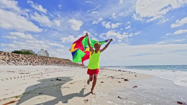 Action photo of boy run with color fabric on ocean beach