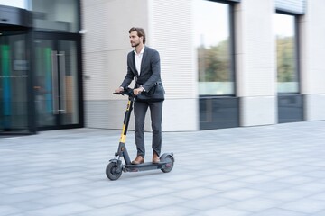 Young business man in a suit riding an electric scooter on a business meeting. Ecological transportation concept.