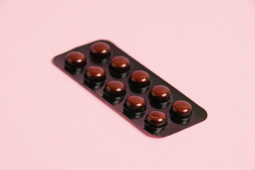 Pills in brown blister pack on pink paper background with copy space.