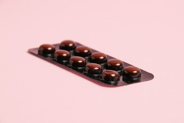 Pills in brown blister pack on pink paper background with copy space.