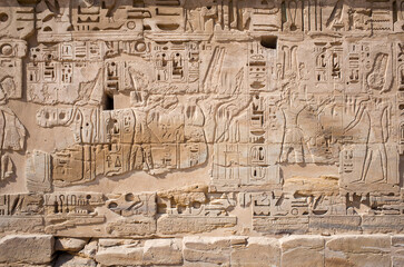Sandstone wall with images of ancient Egyptian symbols, hieroglyphs, gods and pharaohs, detail of a bas-relief in the Temple of Medinet Habu in Luxor, Egypt - obrazy, fototapety, plakaty