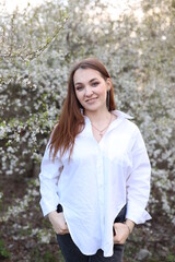 beautiful girl in a white shirt near a blooming tree. Beautiful warm spring and blossoming trees