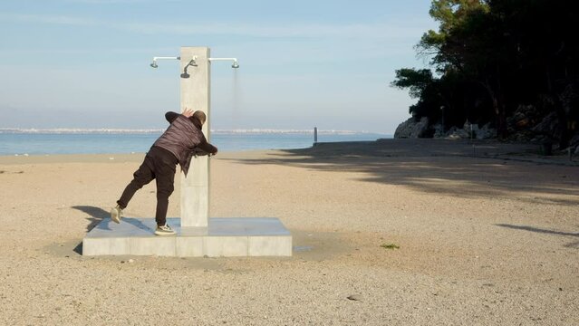 man runs to shower rack on beach and turns off water. Waste of water, person takes care of environment and stops senseless flow of water on beach.