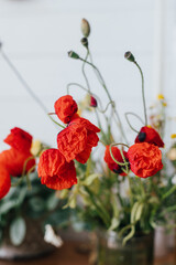 Beautiful poppy flowers on rustic table in sunny room. Gathering and arranging flowers at home in countryside. Red poppy flowers in glass vase