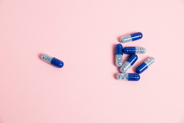 Blue pills on pink paper background with copy space, flatlay. Vitamins in tablet form