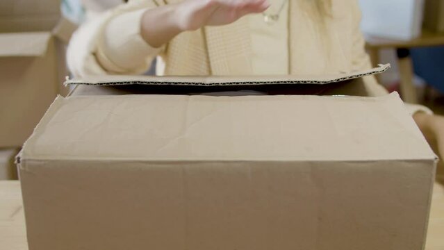 Young Caucasian lady closing cardboard parcel and preparing it for delivery. Closeup of female hands preparing box for shipment using scotch tape. Cropped shot. Startup, small business concept