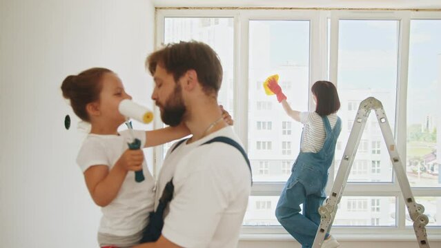 Joyful young Caucasian family painting room. Dad teaching little adorable daughter to paint wall using roller brush. Family time together with their young daughter father, paint a wall with a roller