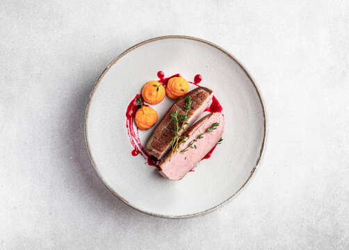 Roast duck breast with carrot cream and berry sauce on a light background, top view