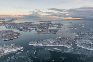 Top view of the snow-covered Soukka Islands in Espoo. Sunset on a winter day. There is ice on the water in places. Winter landscape. Scandinavia.