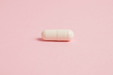 One white medical capsule on a pink background with copy space