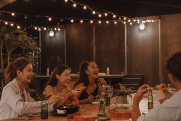 Young Asian friends eating and enjoying dinner together at outdoor restaurant. Friendship and reunion celebration