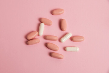 Pink pills and white medical capsules on pink paper background with copy space. The concept of...