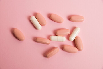 Pink pills and white medical capsules on pink paper background with copy space. The concept of taking vitamins in tablet form