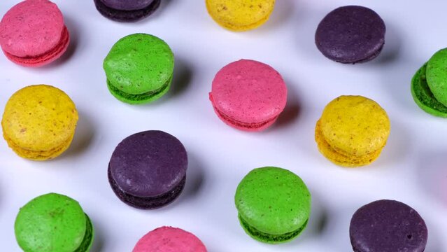 Rotating background of sweet macaroon cookies in different colors on a pink background