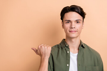 Fototapeta premium Photo of cool handsome optimistic guy with brunet hair dressed khaki shirt indicating empty space isolated on beige color background