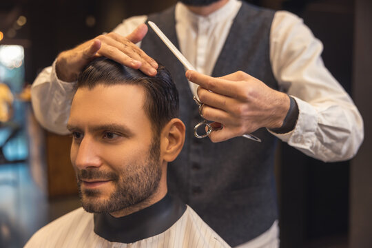 Male hairdresser combing the clients hair in the babershop