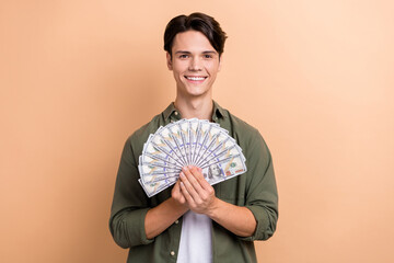 Portrait of cheerful satisfied man arms hold dollar banknotes bills isolated on beige color background