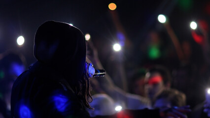 Fans Raise Hands and takes a photos in Front of Bright Colorful Strobing Lights at a concert in a night club.