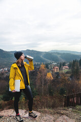 Woman wearing glasses and yellow jacket working on laptop outdoors surrounded by beautiful nature, forest and mountains. Workation concept. Freelancer work, remote work