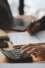 Businessman using a calculator to calculate numbers on a company's financial documents, he is...