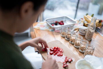 A young woman is cutting strawberries to prepare fitness yogurts with cereal for a picnic