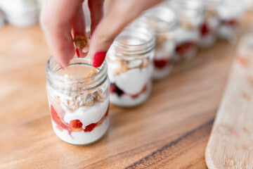 A young woman is dropping cereals to make a fitness yogurt with strawberries in a small jar