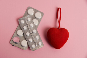 Opened blisters with pills and a red heart on a pink background. Concept of treatment of heart...