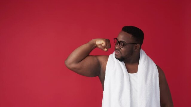 Man strength. Body positive. Masculine power. Confident satisfied chubby guy in glasses showing strong arm biceps muscles on red copy space background.