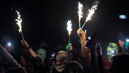 Fans Raise Hands with glowing sparklers in Front of Bright Colorful Strobing Lights on Stage.