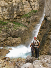 father and daughter trekking near waterfall in Italy Dolomites