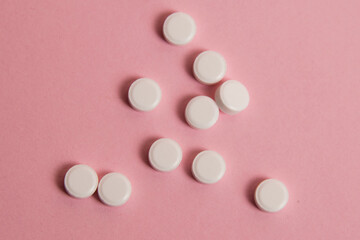Flatlay, many white pills on a pink paper background