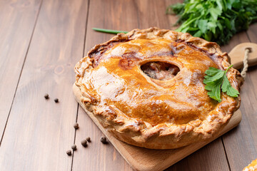 Homemade meat pie with greenery on wooden background