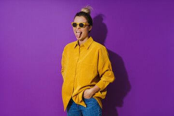 Young cheerful girl wearing yellow shirt and sunglasses against purple background