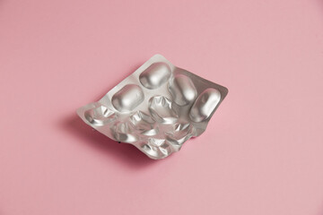 Pills in a gray blister on a pink paper background. Concept of treatment of diseases and support of...