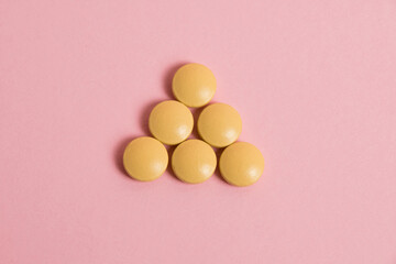 Fototapeta na wymiar Yellow vitamins in pills on a pink paper background. Concept of immunity support in spring.