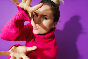 Young woman in wearid pose wearing warm polo neck sweater against purple background