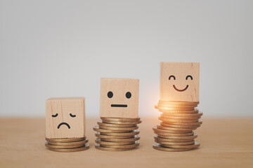 wooden cube block with emotion face on stack of coins, saving money, deposit, wealthy, profit, cash for health budget or insurance concept