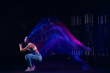 Portrait of muscular strong sportive young girl doing exercises, workout at dark gym in mixed neon...